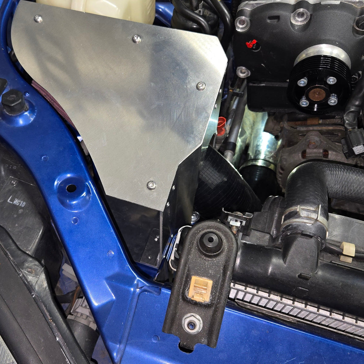 Close engine-bay view of the cold-air intake enclosure cover beside the supercharger pulley and inlet hose
