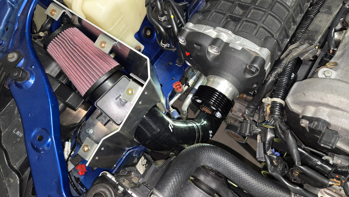 Close engine-bay view of the coldside cone filter, airflow meter, aluminum enclosure, inlet hose, and supercharger pulley