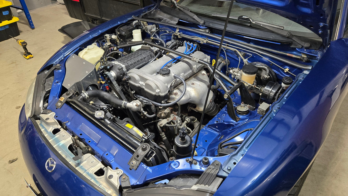 Angled overview of a 1999–2005 Miata engine bay showing the installed FFS supercharger and coldside intake enclosure