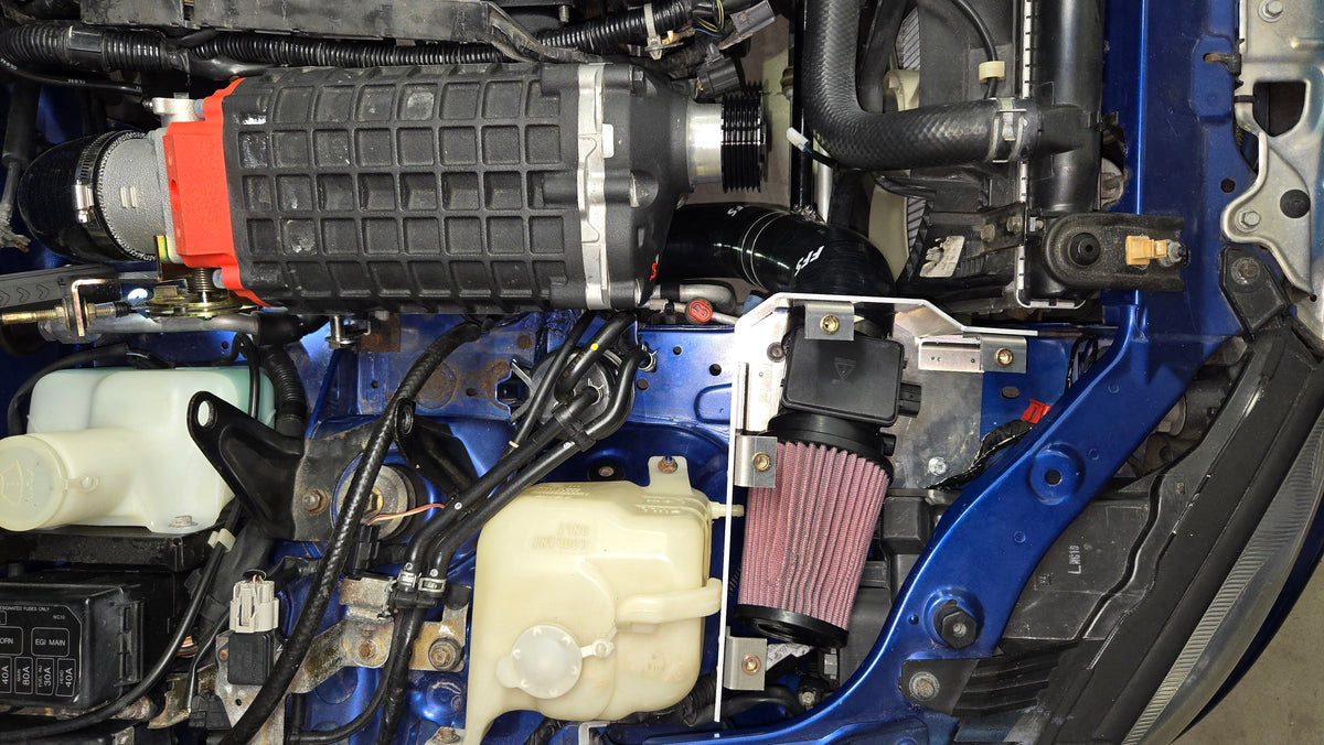 1999–2005 Miata engine-bay view showing the supercharger, open cold-air intake enclosure, cone filter, and airflow meter