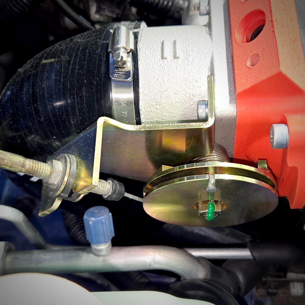 Side view of the throttle cable bracket upgrade installed below the throttle body, showing the cable-adjustment hardware