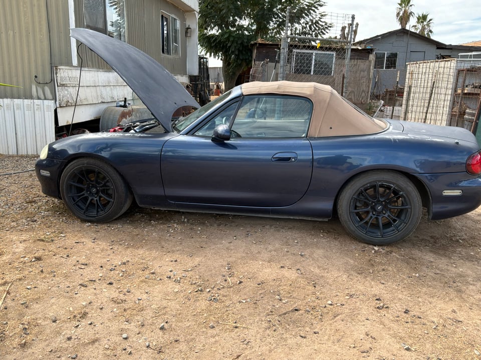 Side view of Nathaniel's blue 2001 Miata with tan soft top and hood open